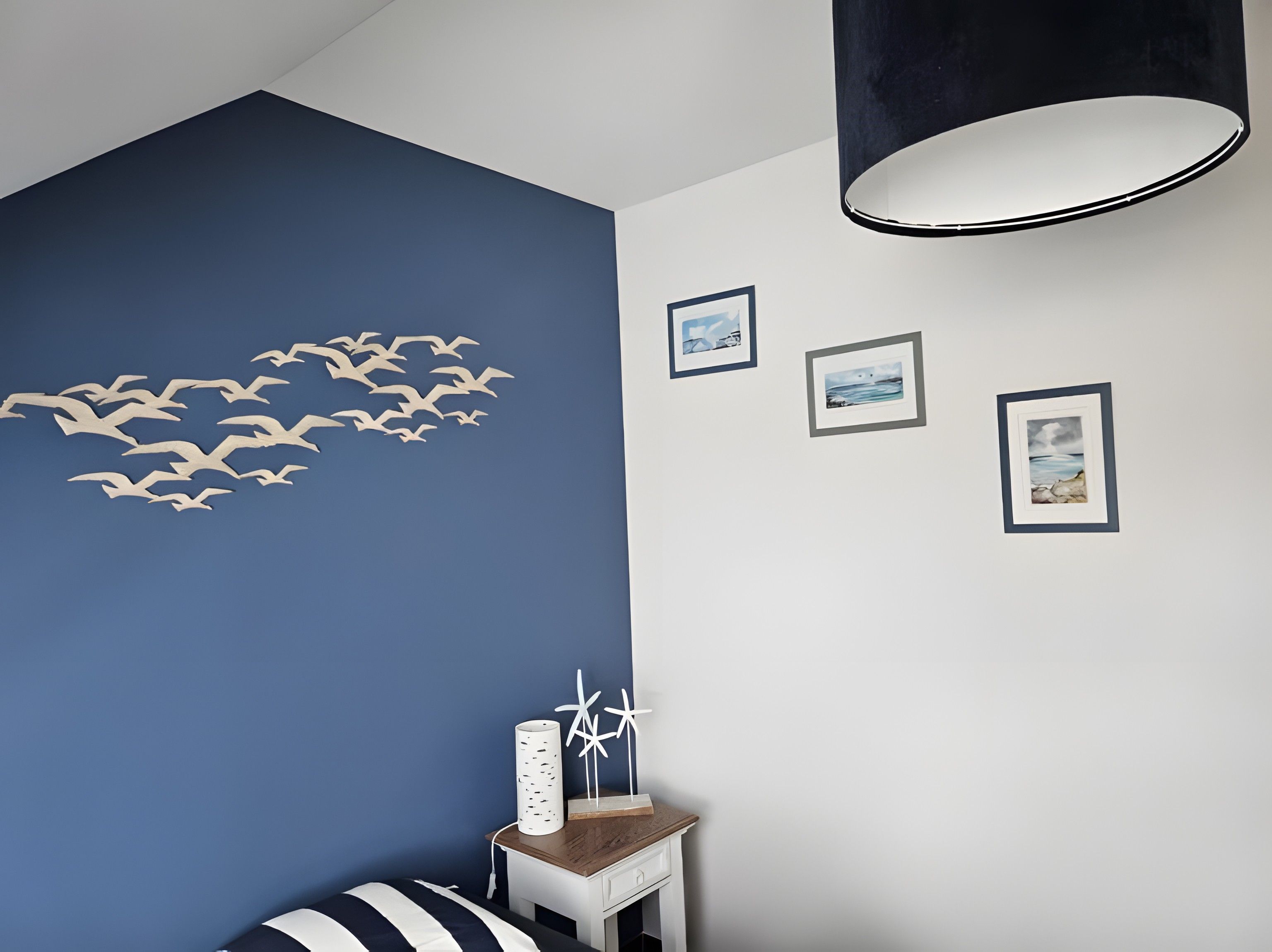 Une pièce avec un mur d’accent bleu, un plafond blanc et un luminaire suspendu noir. Trois tableaux encadrés sont accrochés au mur.
