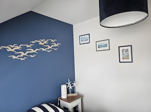 Una habitación con una pared azul de acento, techo blanco y una lámpara colgante negra. Hay tres cuadros enmarcados en la pared.