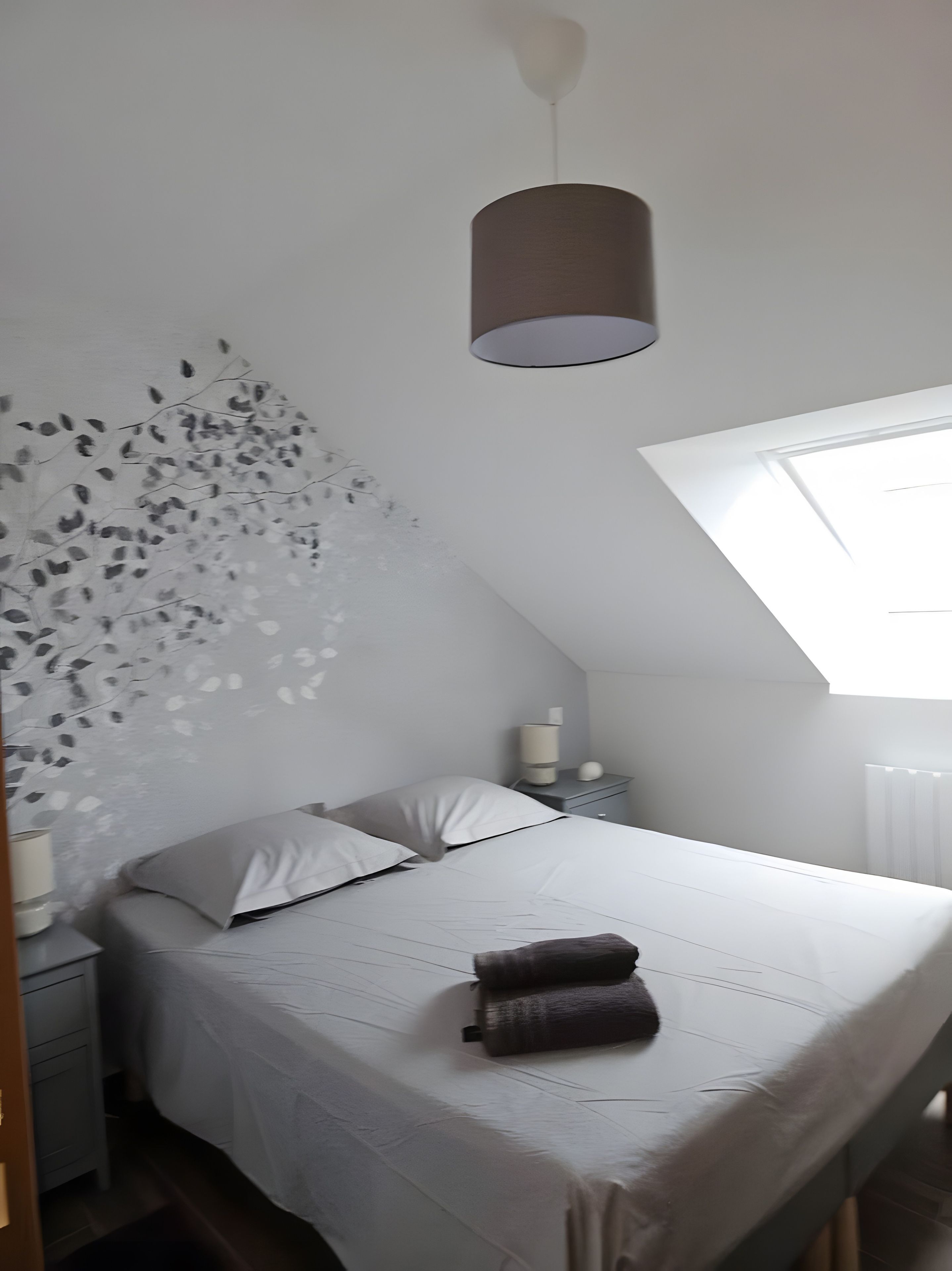 Een slaapkamer met een bed, een nachtkastje, een lamp en een muur met een bladmotief.