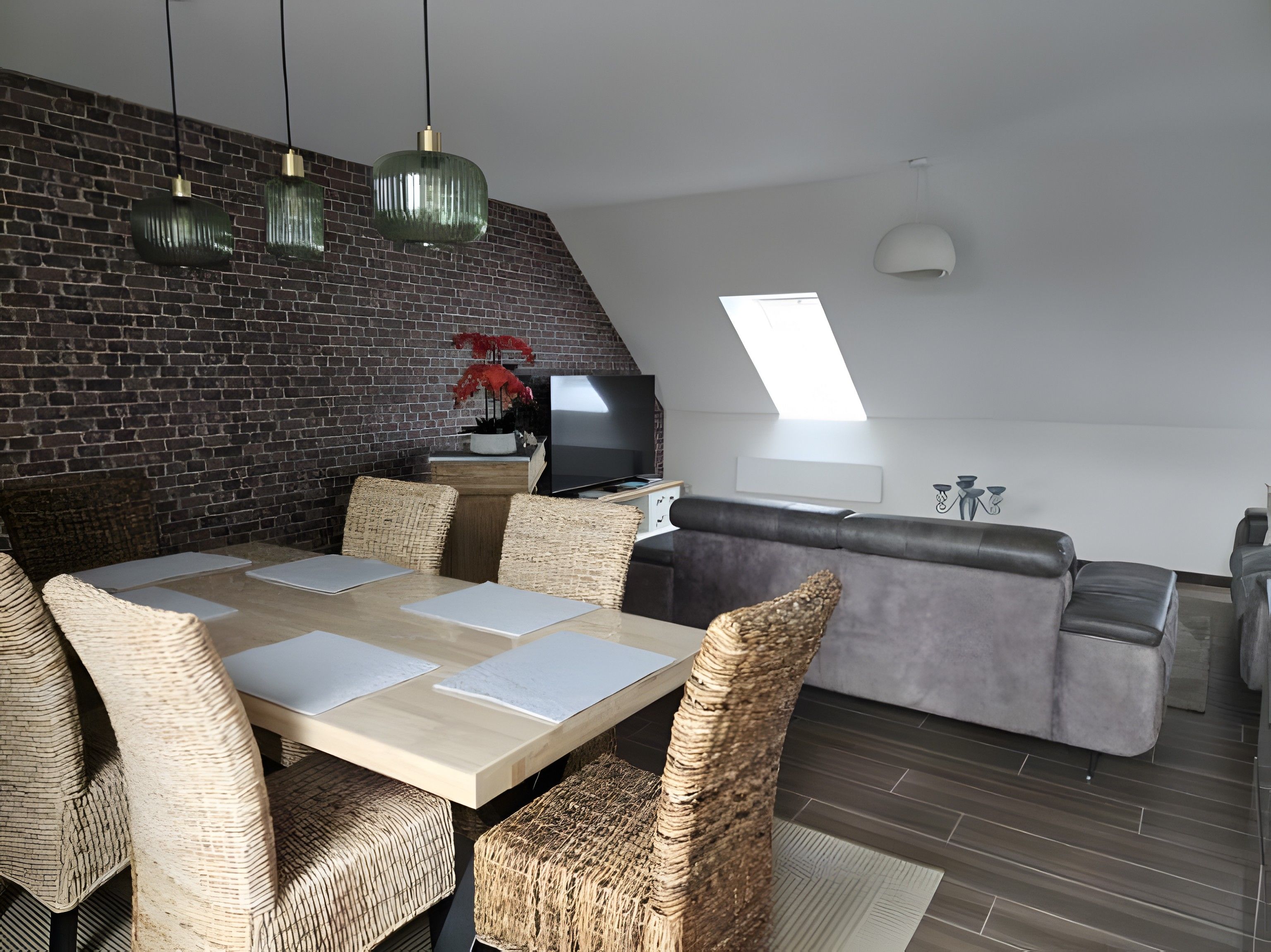 Een moderne woonruimte met een eethoek, een bank, een televisie en een bakstenen muur.