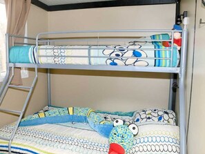 Ein Stockbett mit einer Leiter, ein Fenster mit Vorhängen und ein Stofftier auf dem oberen Bett.