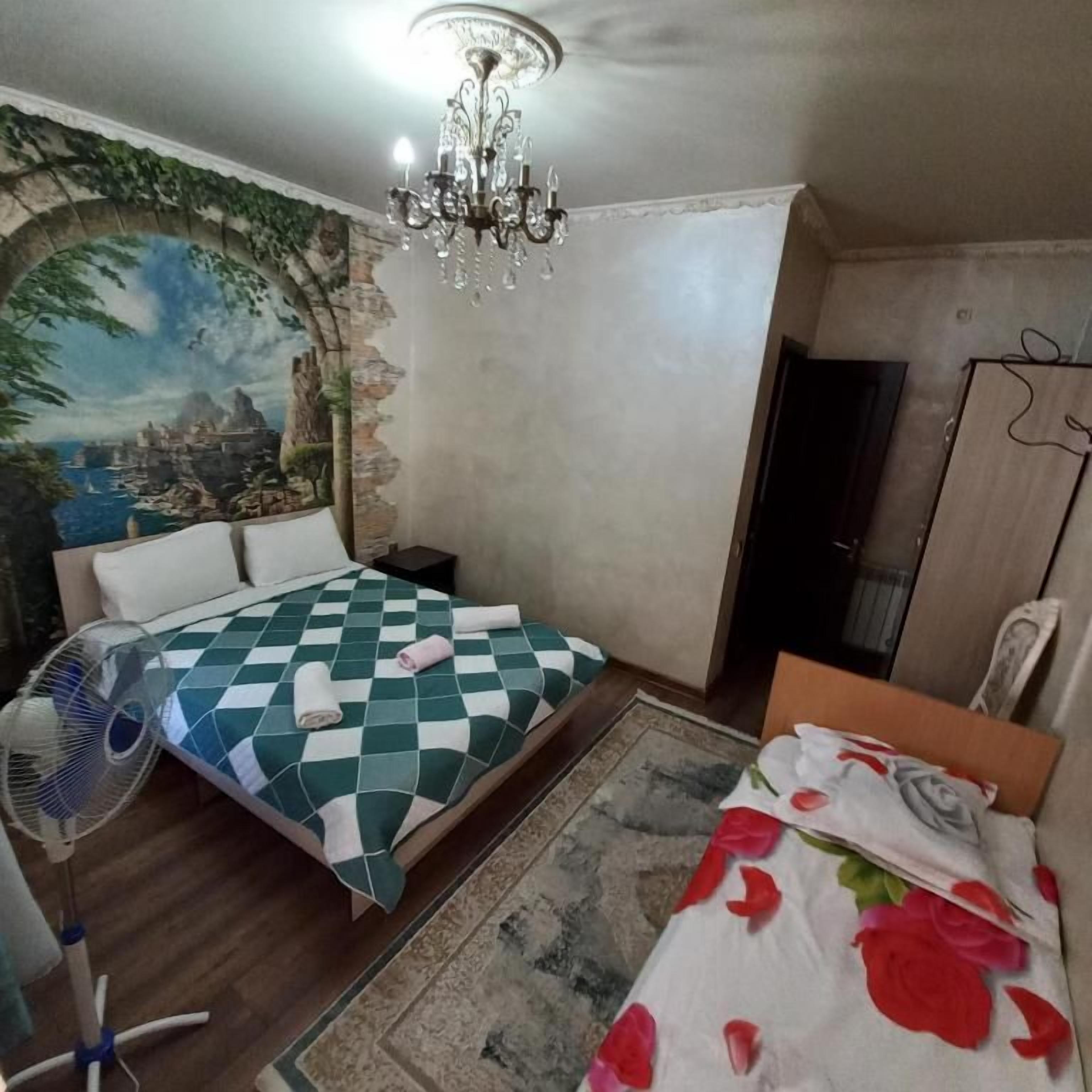 A bedroom with a bed, a fan, a chandelier, and a wall mural.
