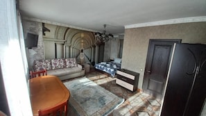 A room with a sofa, a dining table, a chandelier, and a patterned rug. - Camelot (Bishkek)
