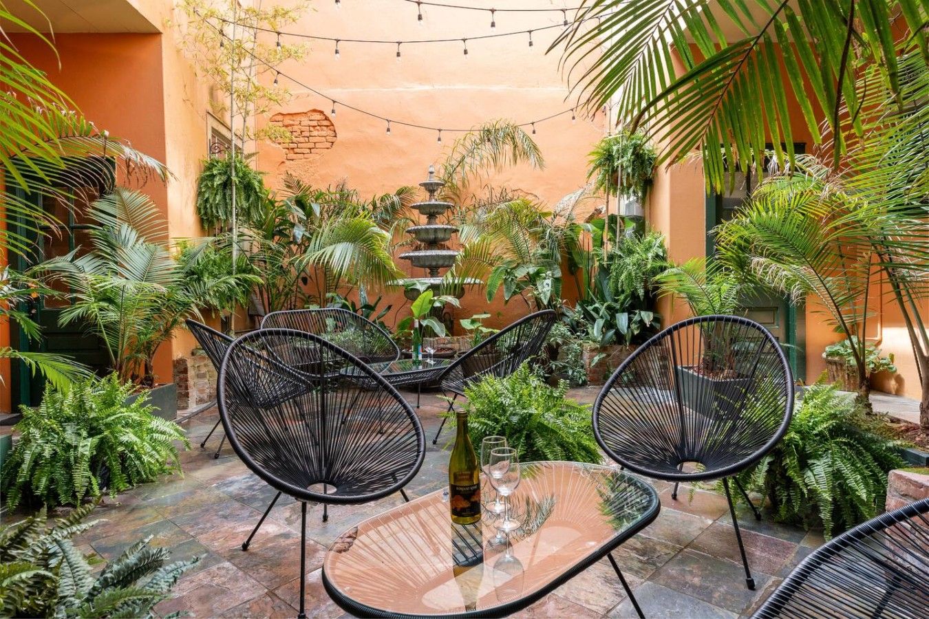 An outdoor patio area with black wicker chairs, a glass table, and a fountain.