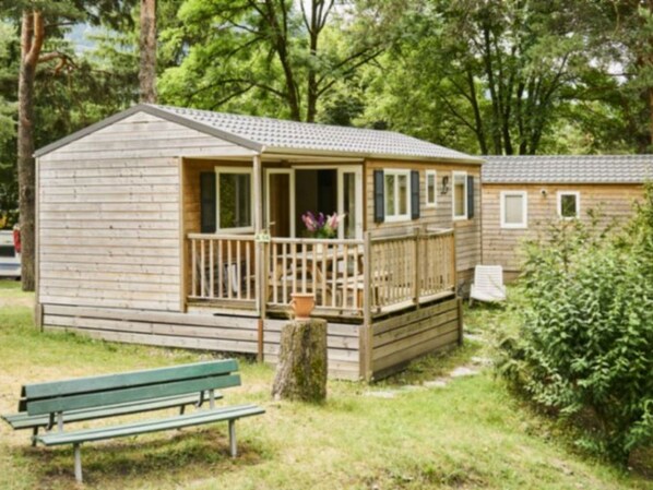 A small wooden cabin with a porch, a bench, and a tree in front. - Mobile home with terrace - 6 guests (Séez)