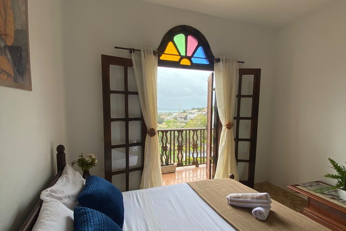 Ein Schlafzimmer mit Bett, einem fensterbeprägten Fenster, einem Deckenventilator und Blick ins Freie.