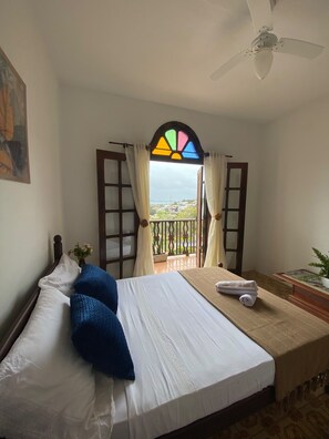 Ein Schlafzimmer mit Bett, einem fensterbeprägten Fenster, einem Deckenventilator und Blick ins Freie.