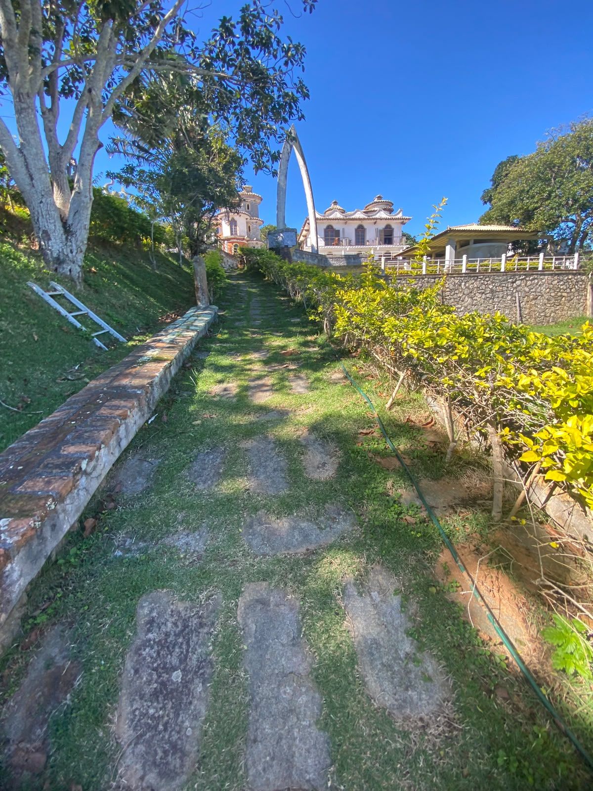 Uma trilha leva a um edifício com arquitetura tradicional, cercado por vegetação e árvores.