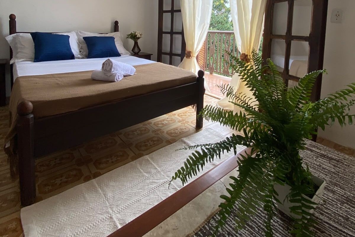 Ein Schlafzimmer mit einem Bett, einem Deckenventilator, einem Fenster mit Vorhängen und einer Pflanze.