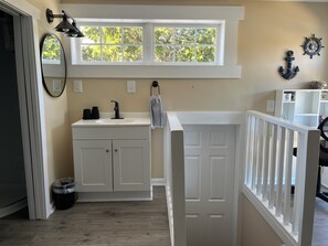 Une salle de bain avec une fenêtre, un lavabo, des placards, une serviette et une porte.