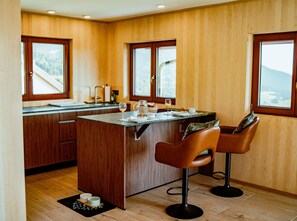 A kitchen with wooden cabinets, a central island, bar stools, and a view of the outdoors through large windows.