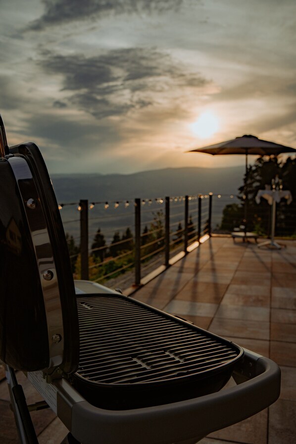 A grill on an outdoor patio with a view of the sunset and distant mountains.