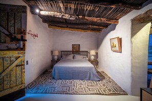 A bedroom with a bed, two bedside tables, a nightstand, a wall-mounted picture, and a patterned rug. - Architect Design 1-bedroom cabin in the Klein Karoo South Africa - Pet Friendly. (Oudtshoorn)