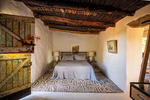 A bedroom with a bed, two bedside tables, a nightstand, a wooden door, and a wall-mounted picture. - Architect Design 1-bedroom cabin in the Klein Karoo South Africa - Pet Friendly. (Oudtshoorn)