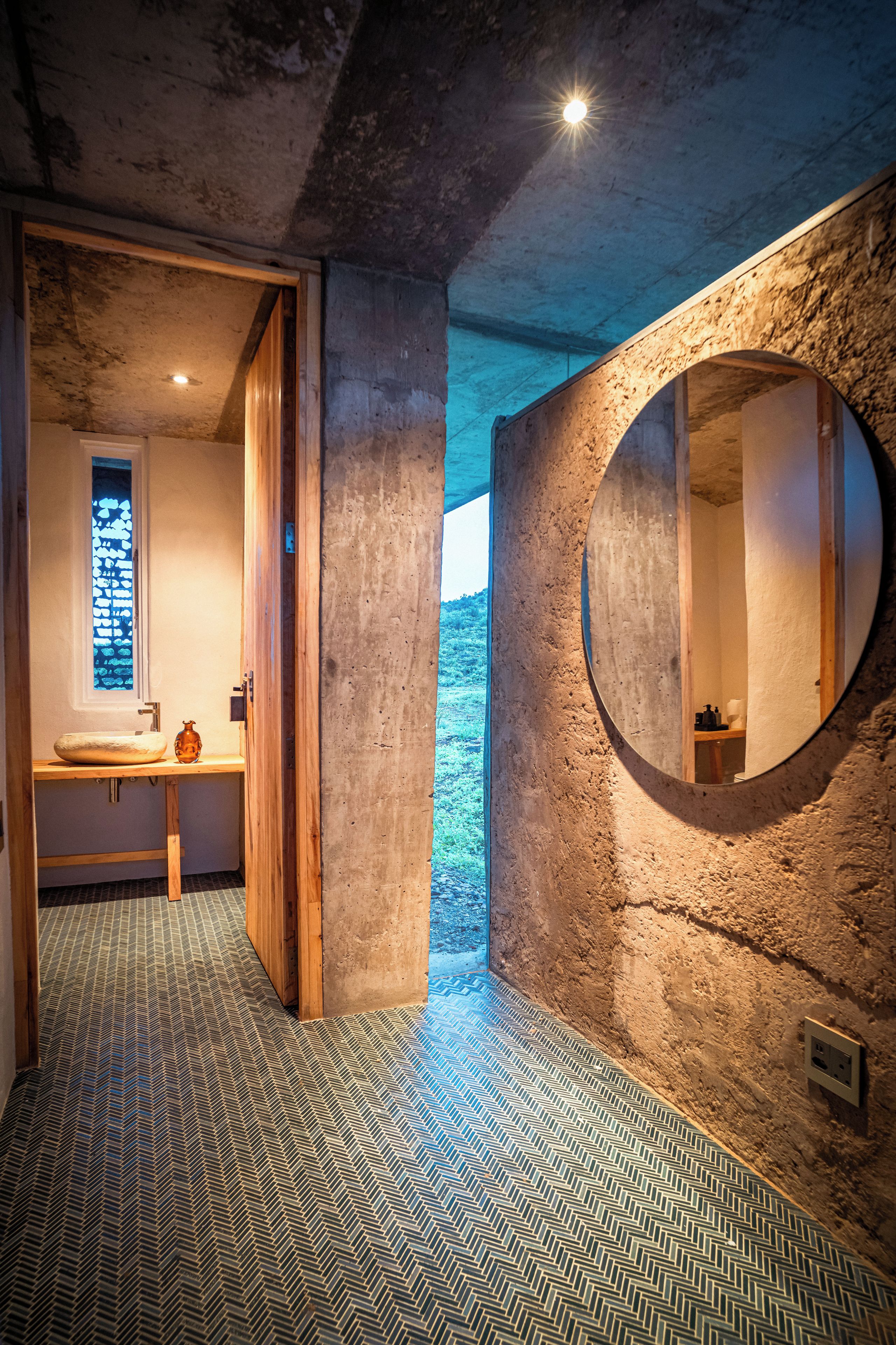 A bathroom with a wooden vanity, a round mirror, and a patterned floor.
