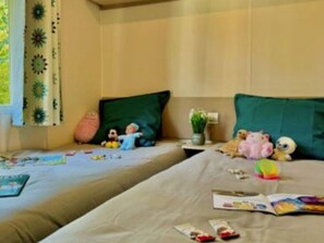 Ein Hotelzimmer mit zwei Betten, einem Fenster mit Vorhängen, einem Nachttisch mit Pflanze und Stofftieren auf den Betten.