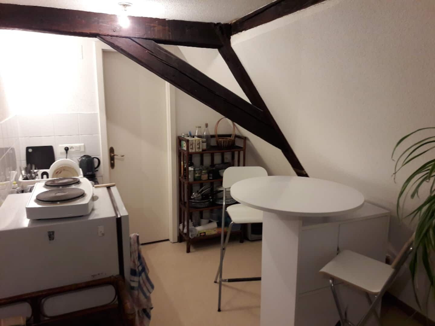 A compact kitchen with a white countertop, a coffee maker, and a small dining area with a white table and chairs.