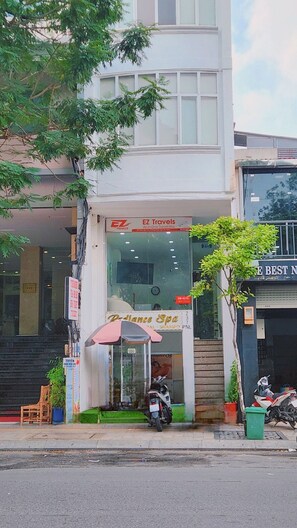 A building with a glass entrance, a sign for EZ Travels, and a small kiosk with a pink umbrella. - D1 Heart · Rooftop & Kitchen · Peony @ Cozinema (Ben Thanh, District 1)