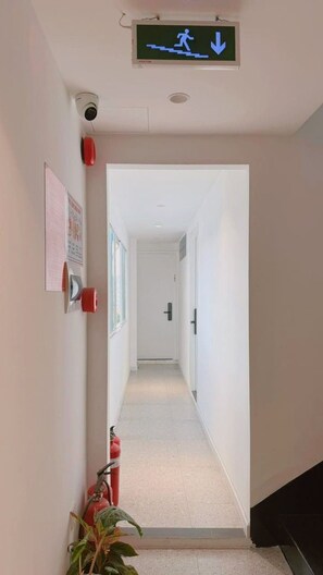 A hallway with a fire exit sign, a security camera, a fire extinguisher, and a door at the end. - D1 Heart · Rooftop & Kitchen · Peony @ Cozinema (Ben Thanh, District 1)