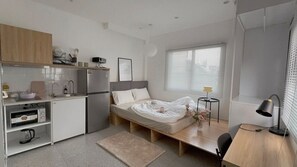 Une pièce compacte comprenant un coin cuisine, un lit, un bureau et une fenêtre.