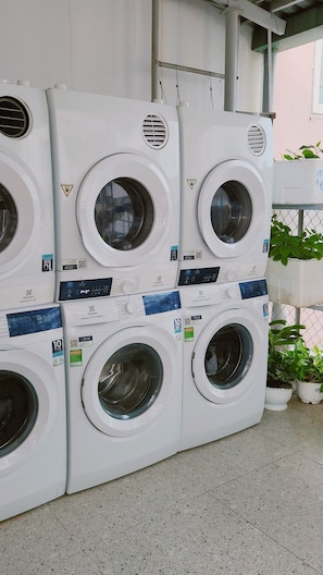 A row of stacked front-loading washing machines with control panels and safety labels. - D1 Heart · Rooftop & Kitchen · Peony @ Cozinema (Ben Thanh, District 1)