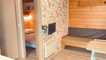 Une pièce confortable avec un lit, un banc et un téléviseur fixé au mur.