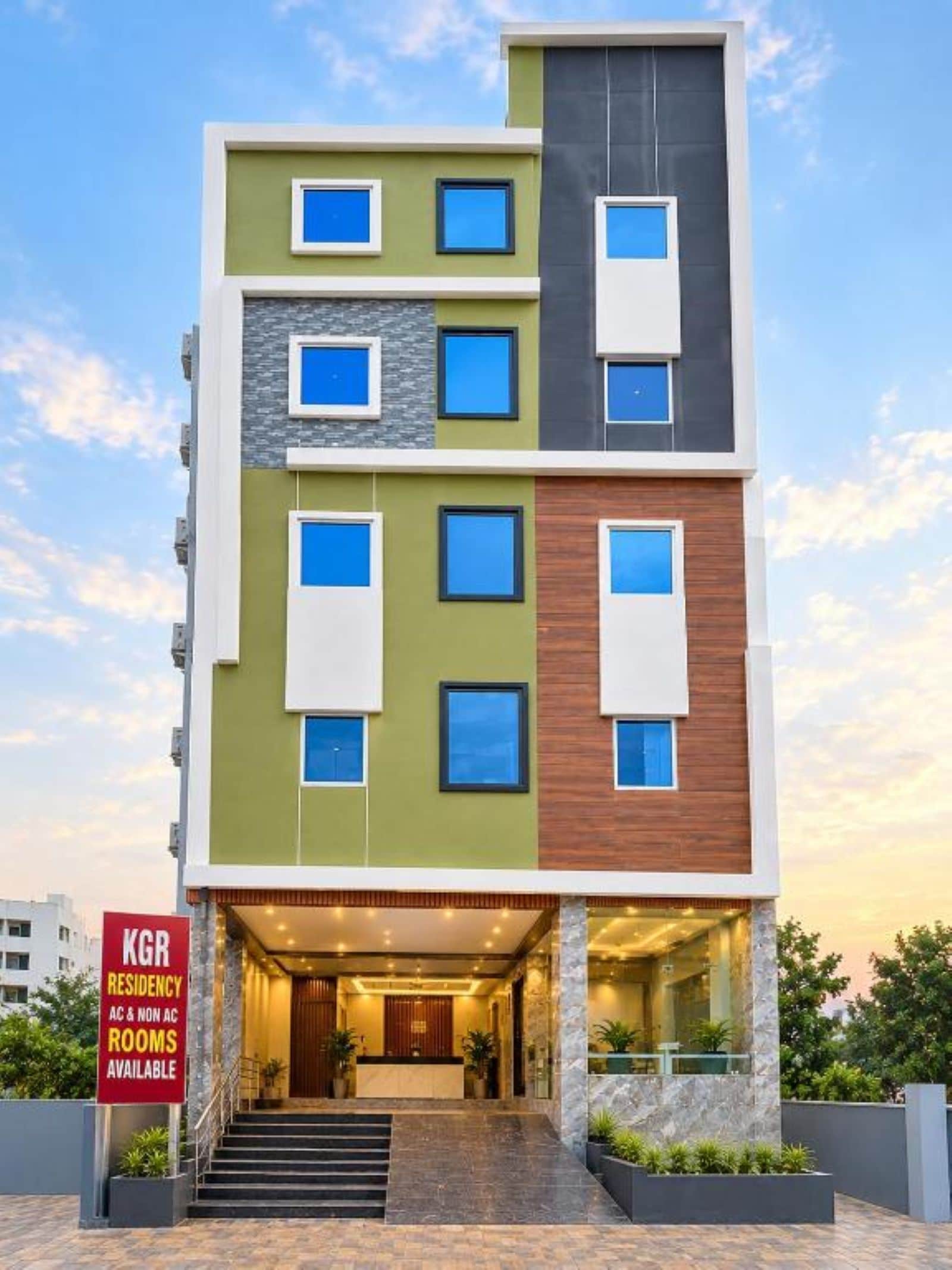 A multi-story building with a modern design, featuring a mix of green, grey, and brown facades, and a sign indicating KGR Residency with AC and non-AC rooms available.