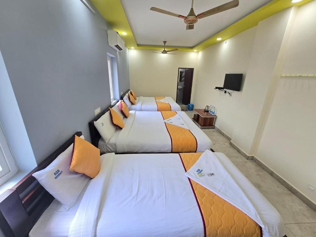 A hotel room with three beds, a ceiling fan, a flat-screen TV, and a small table with a water bottle.