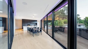 Una cocina moderna con una isla central, un comedor con mesa y sillas, y un gran ventanal corredizo que da a una terraza exterior.