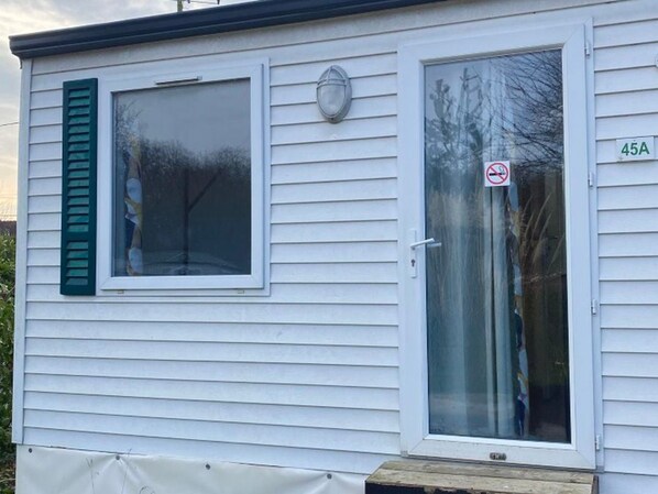 A single-story mobile home with a window and a door, a mailbox, and a house number sign. - Mobile home with AC - 2 guests, pets allowed (Angicourt)