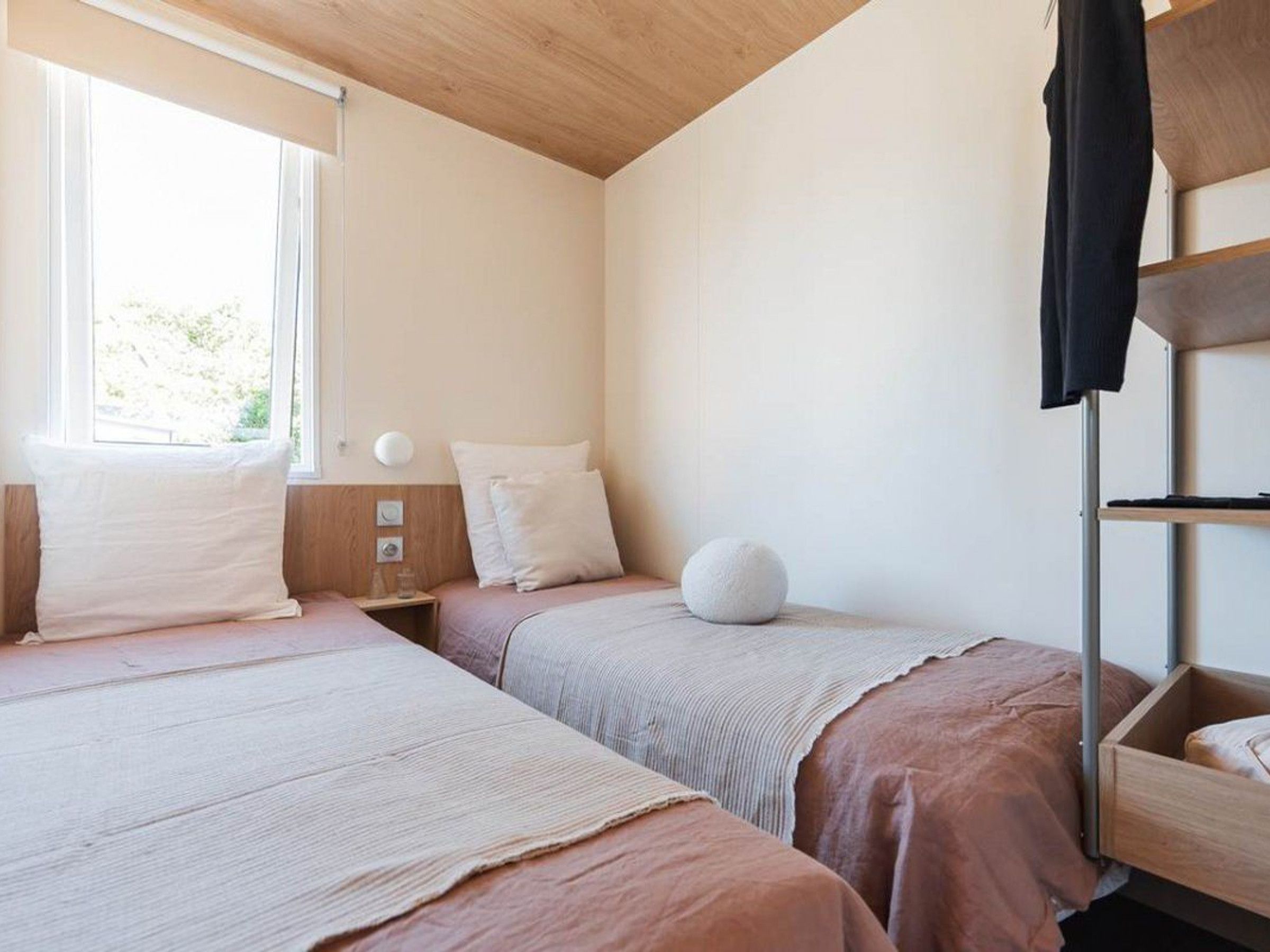 A bedroom with two beds, a window, a bedside table, and a wardrobe.