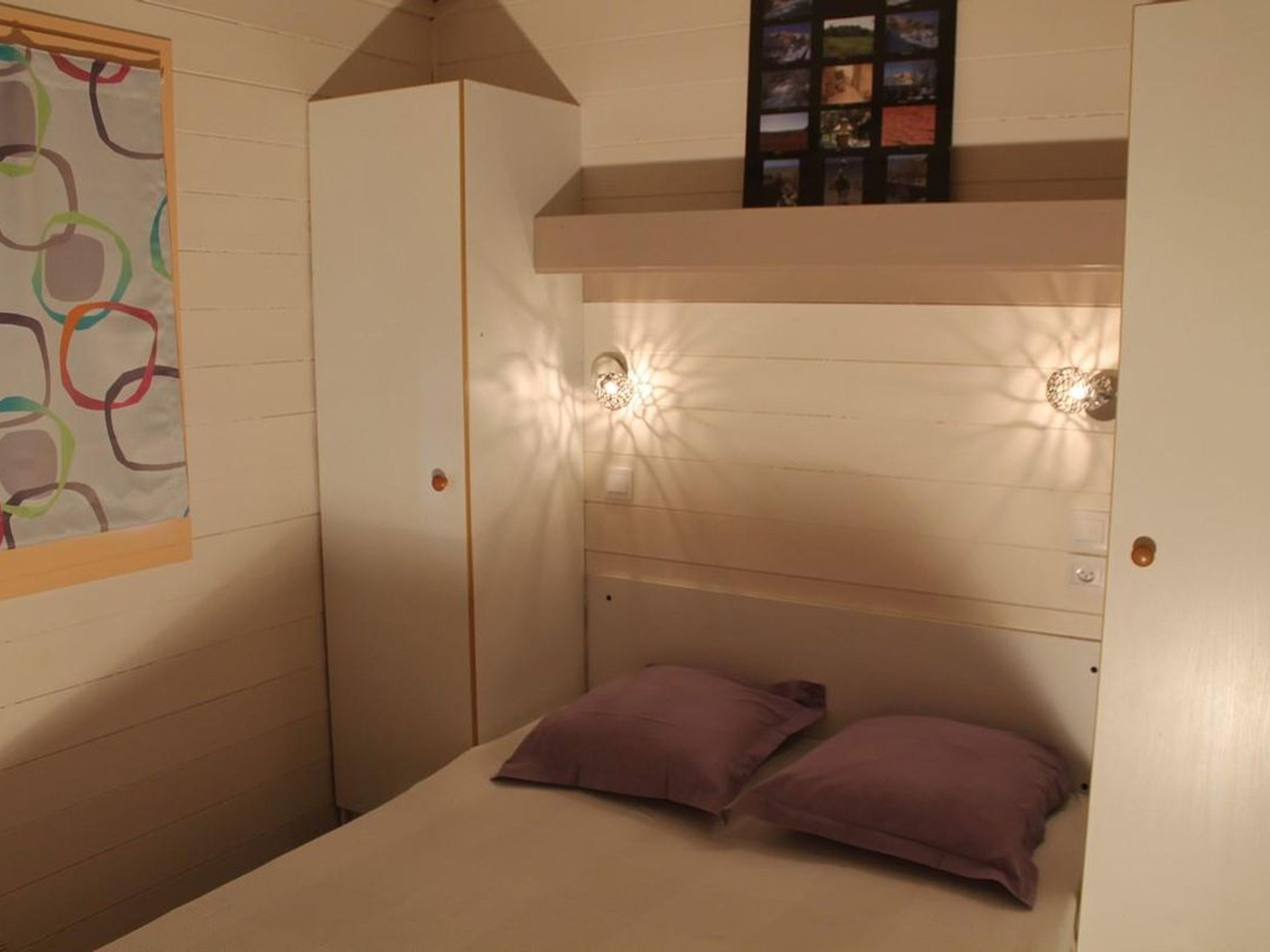 Une chambre avec un lit superposé, une armoire et une étagère murale décorée de tableaux.