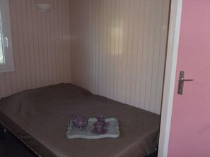 A small room with a single bed, a door, and a window.