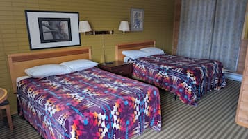 A hotel room with two beds, a wooden headboard, a nightstand, a framed picture, and a patterned curtain.
