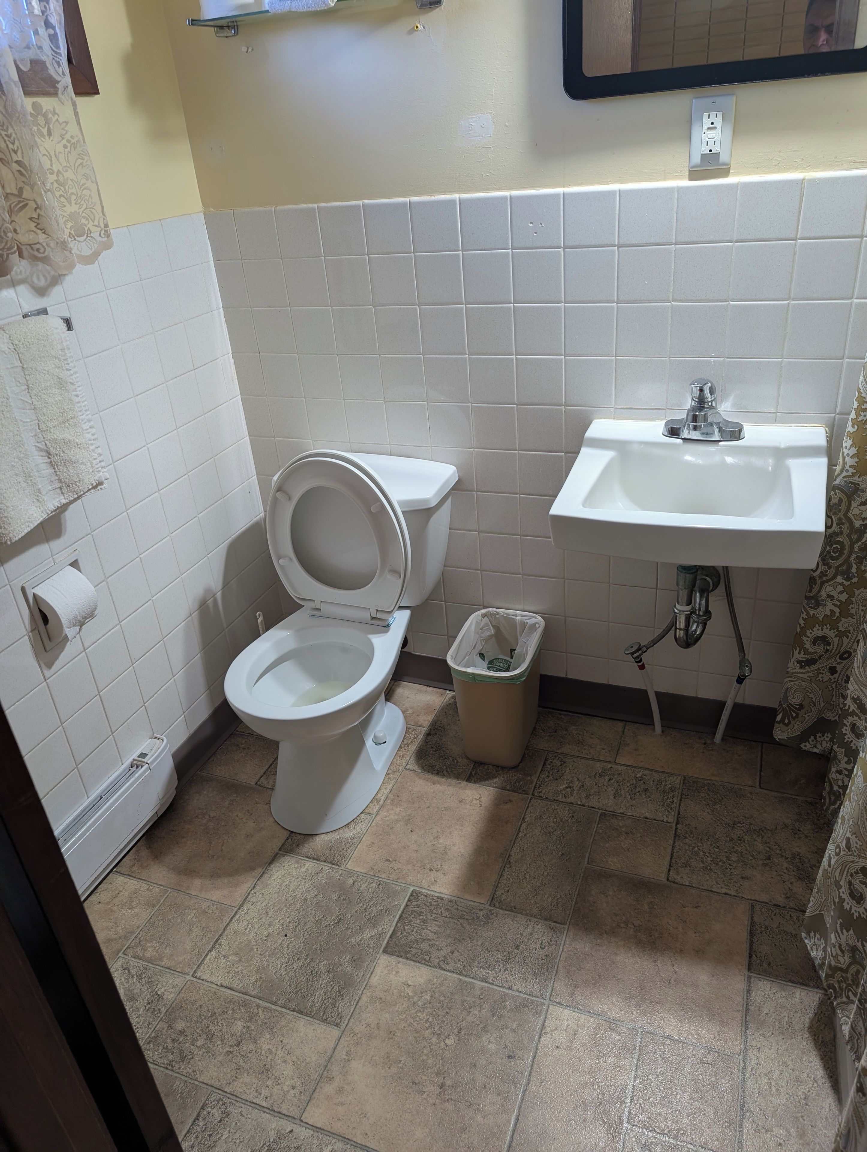 A bathroom with a toilet, a sink, a trash bin, and a towel rack.