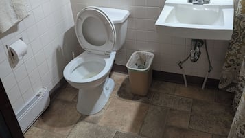 A bathroom with a toilet, a sink, a trash bin, and a towel rack.