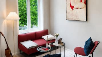 A living room with a red sofa, a white rug, a coffee table, and a painting on the wall.