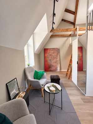 A modern loft with a sloped ceiling, a grey armchair with a green throw, a small round table with a book, and a ladder leading to an upper level. - Modern Private Studio with Loft Central Oslo (Oslo)