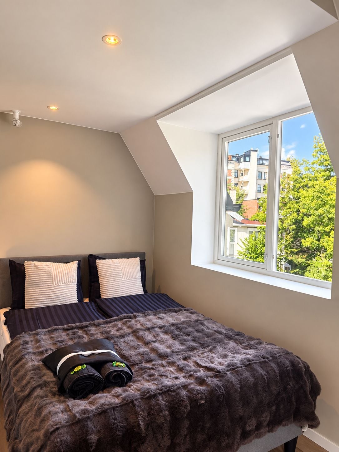 A bedroom with a sloped ceiling, a large window, and a bed with a fluffy blanket.