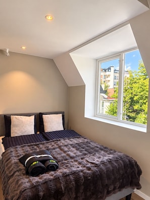 A bedroom with a sloped ceiling, a large window, and a bed with a fluffy blanket. - Modern Private Studio with Loft Central Oslo (Oslo)