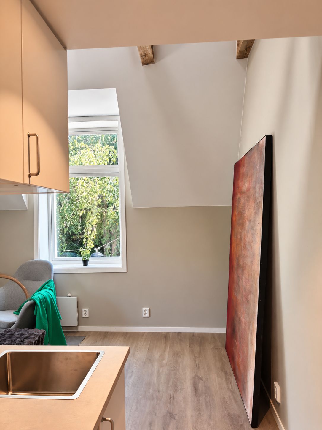 A modern kitchen with a window, a dining area, and a painting on the wall.