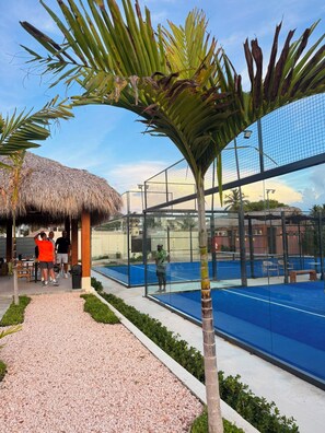 Un'area piscina con recinto in vetro, palme e una struttura con tetto di paglia.