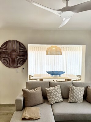 Un soggiorno moderno con un divano componibile, una ventola a soffitto, un elemento decorativo a parete e una zona pranzo con tavolo e sedie.