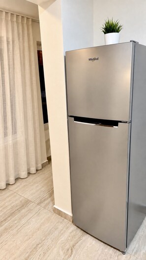Un réfrigérateur Whirlpool en acier inoxydable dans une cuisine moderne, avec un revêtement de sol de couleur claire et un mur blanc.