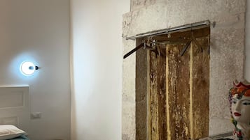 A room with a bed, a stone wall, a wooden door, and a small window.