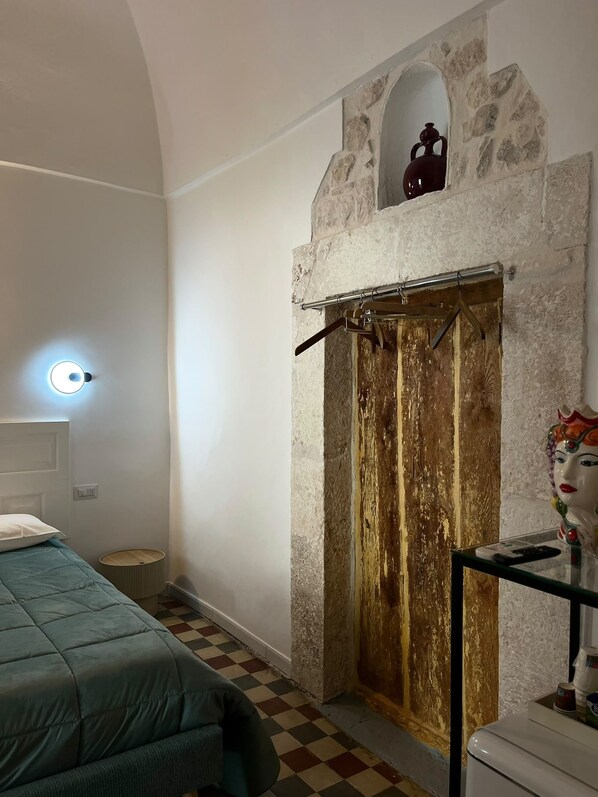 A room with a bed, a stone wall, a wooden door, and a small window. - Room 'Pepenero Apulian Rooms - Cementina' with Balcony, Wi-Fi and Air Conditioning (Noci)