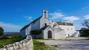 A white church with a bell tower and a stone wall in the foreground. - Room 'Pepenero Apulian Rooms - Cementina' with Balcony, Wi-Fi and Air Conditioning (Noci)