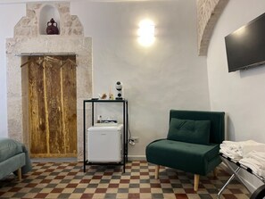 A room with a checkered floor, a green sofa, a small fridge, a coat rack, and a stone wall with a wooden door. - Room 'Pepenero Apulian Rooms - Cementina' with Balcony, Wi-Fi and Air Conditioning (Noci)