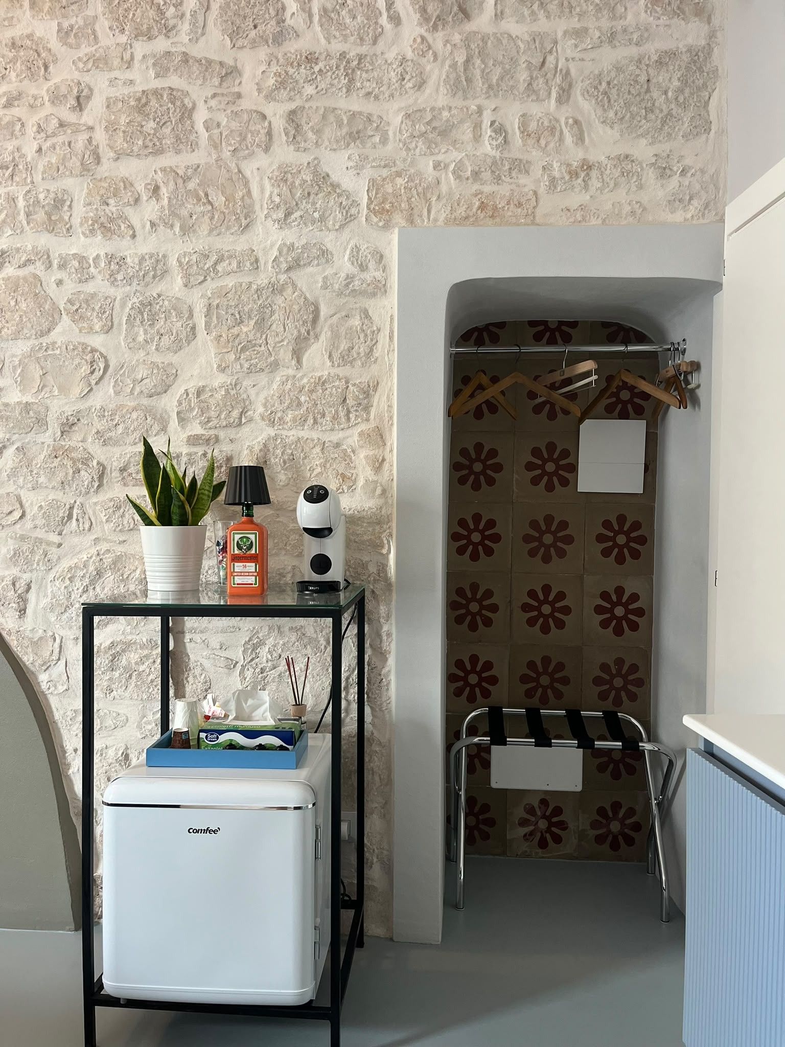 A compact bathroom with a stone wall, a small table with toiletries, a towel rack, and a radiator.
