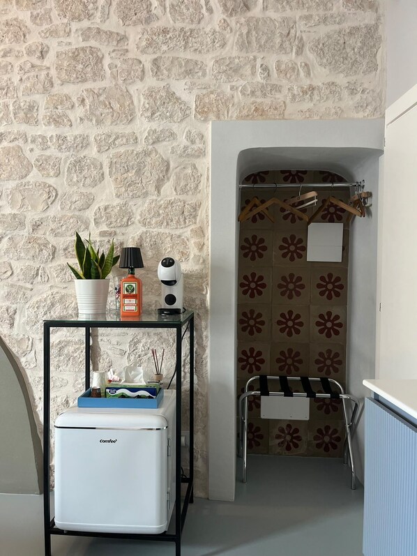 A compact bathroom with a stone wall, a small table with toiletries, a towel rack, and a radiator. - Room 'Pepenero Apulian Rooms - Loggetta' with Wi-Fi and Air Conditioning (Noci)